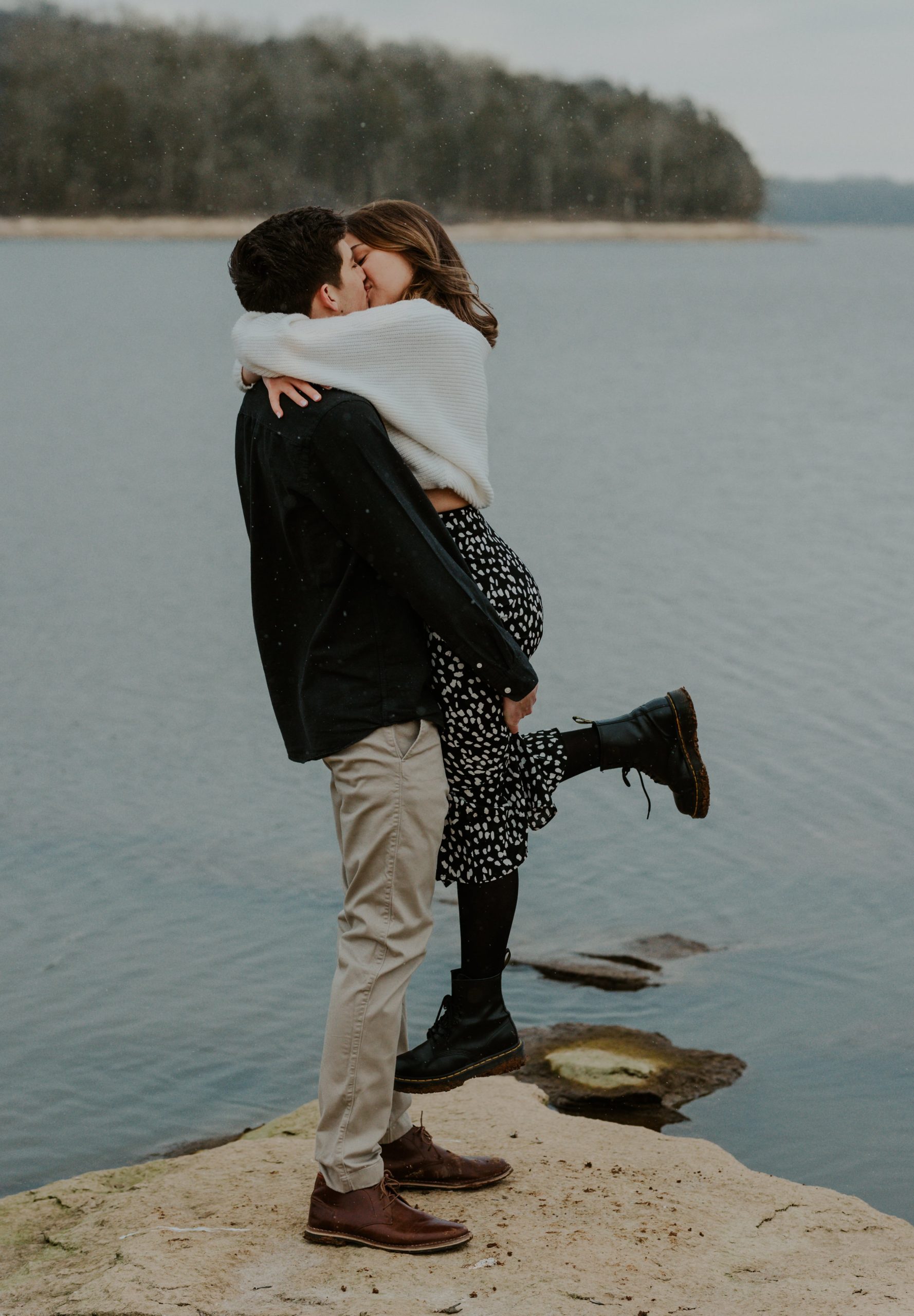 Couple kissing during their engagement at the lake at Long Hunter State Park in the snow.