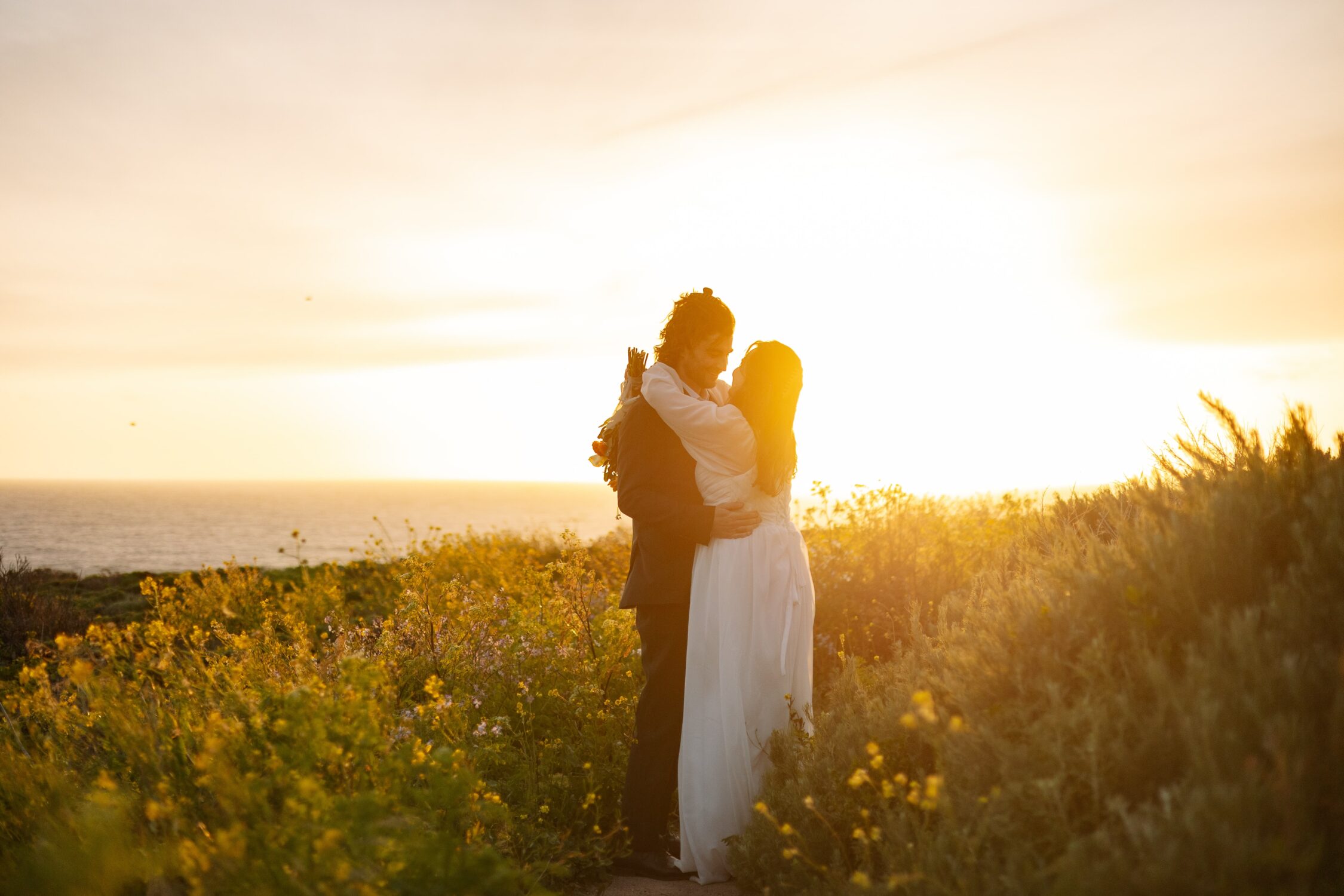 A bride and a groom smile on their elopement in a field of wildflowers on the coastline of Big Sur.